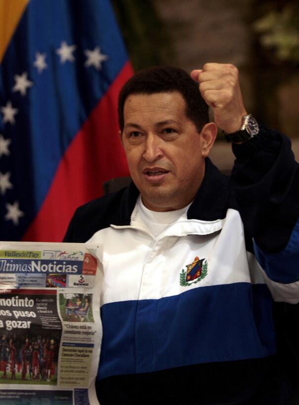 Venezuela's President Hugo Chavez gestures as he holds a newspaper s...